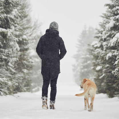 Person walking a dog on a snowy winter trail wearing cold-weather layers